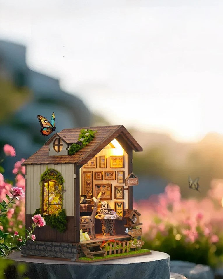 DIY book nook kit “Butterfly Cottage,” featuring a beautiful nature-themed miniature with butterflies, rocking chair, wooden signs, and blooming flowers. A peaceful DIY and crafts project perfect for miniature lovers.