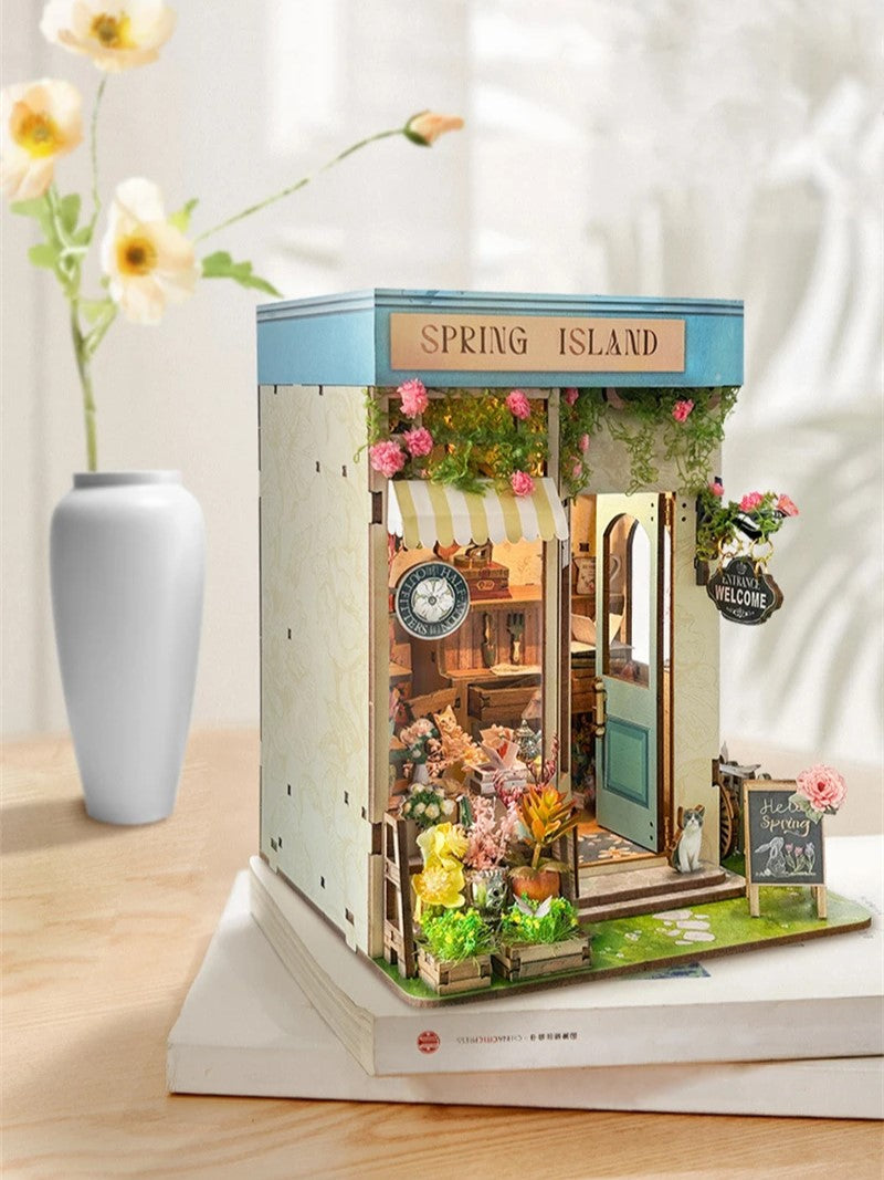 DIY book nook kit “Springkeeper’s Shop” featuring a cheerful miniature flower store with potted plants, blooming flowers, a striped awning, and a small cat. A charming craft idea for DIY and crafts lovers, perfect for fans of miniatures and DIY tiny home kits.