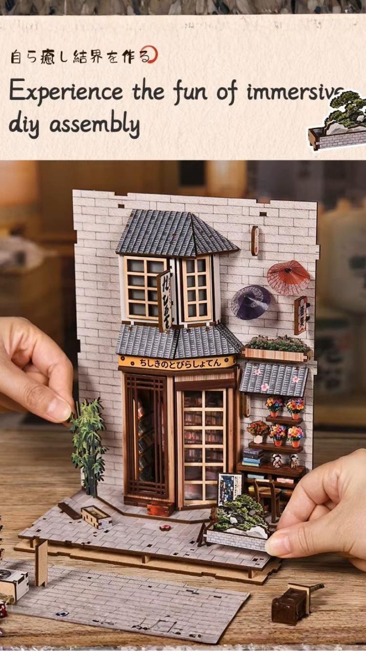 DIY book nook kit “Neko Alley Nook,” featuring a Japanese alleyway with miniature shopfronts, paper lanterns, wooden signage, and lounging cats. A charming DIY and crafts project for Japan enthusiasts and book nook collectors.