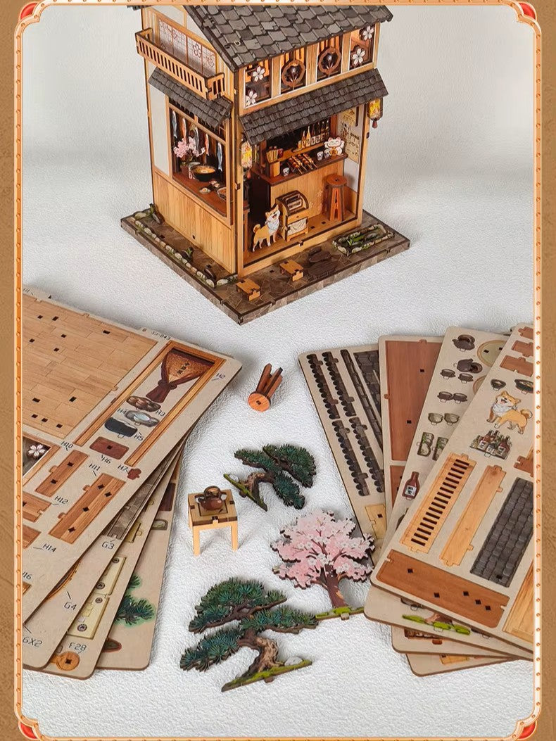 DIY miniature Japanese izakaya house featuring a cat chef, cherry blossom trees, hanging lanterns, a friendly Shiba Inu dog, and a warm glowing interior with tiny food items and sake bottles.