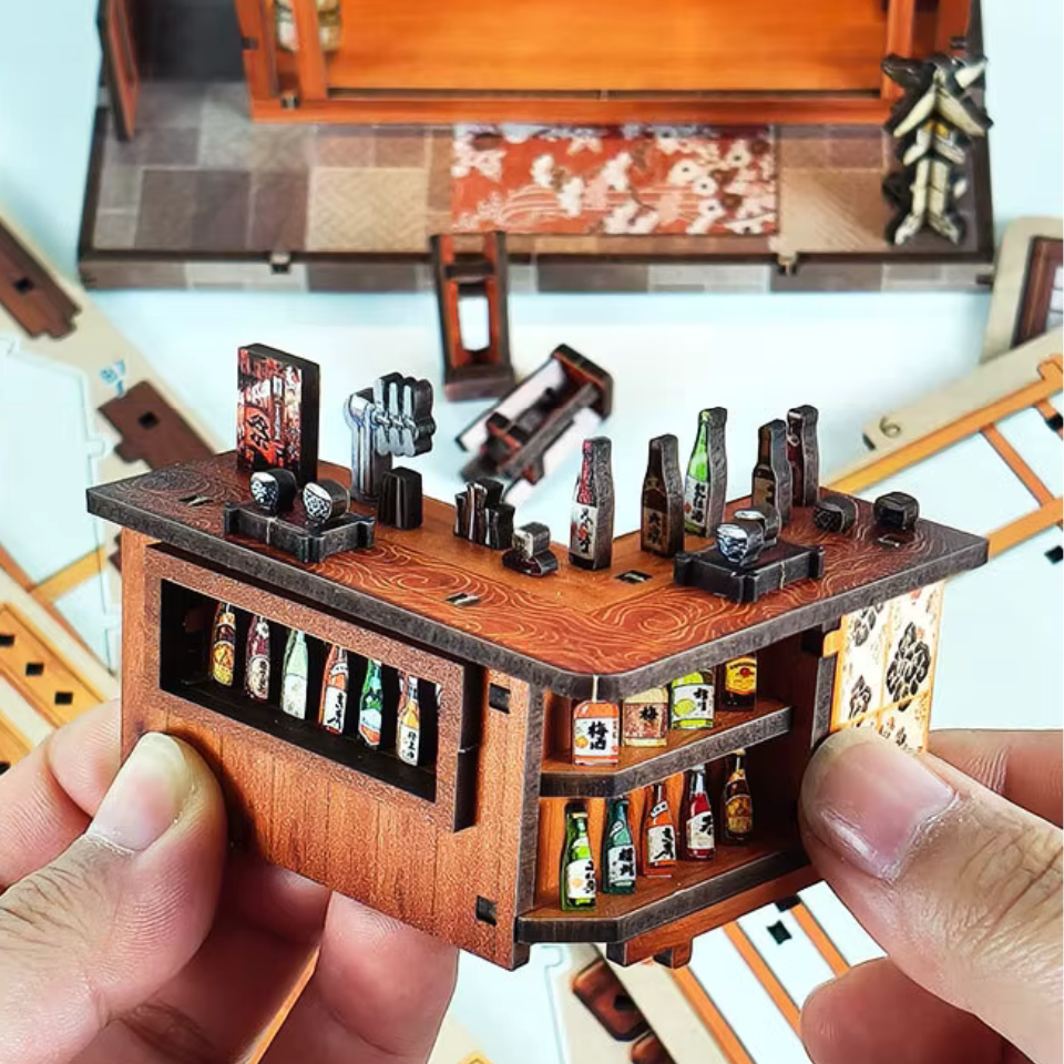 DIY miniature sake bar book nook with glowing lanterns, wooden bar seating, bamboo paneling, and rows of sake bottles, capturing the quiet atmosphere of a late-night Japanese tavern.