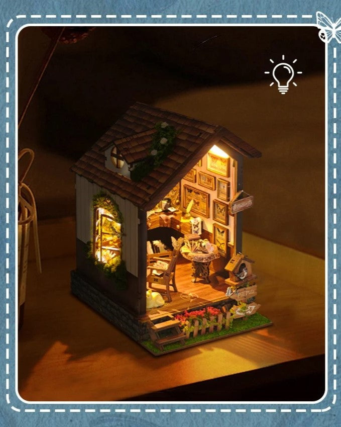 DIY book nook kit “Butterfly Cottage,” featuring a beautiful nature-themed miniature with butterflies, rocking chair, wooden signs, and blooming flowers. A peaceful DIY and crafts project perfect for miniature lovers.