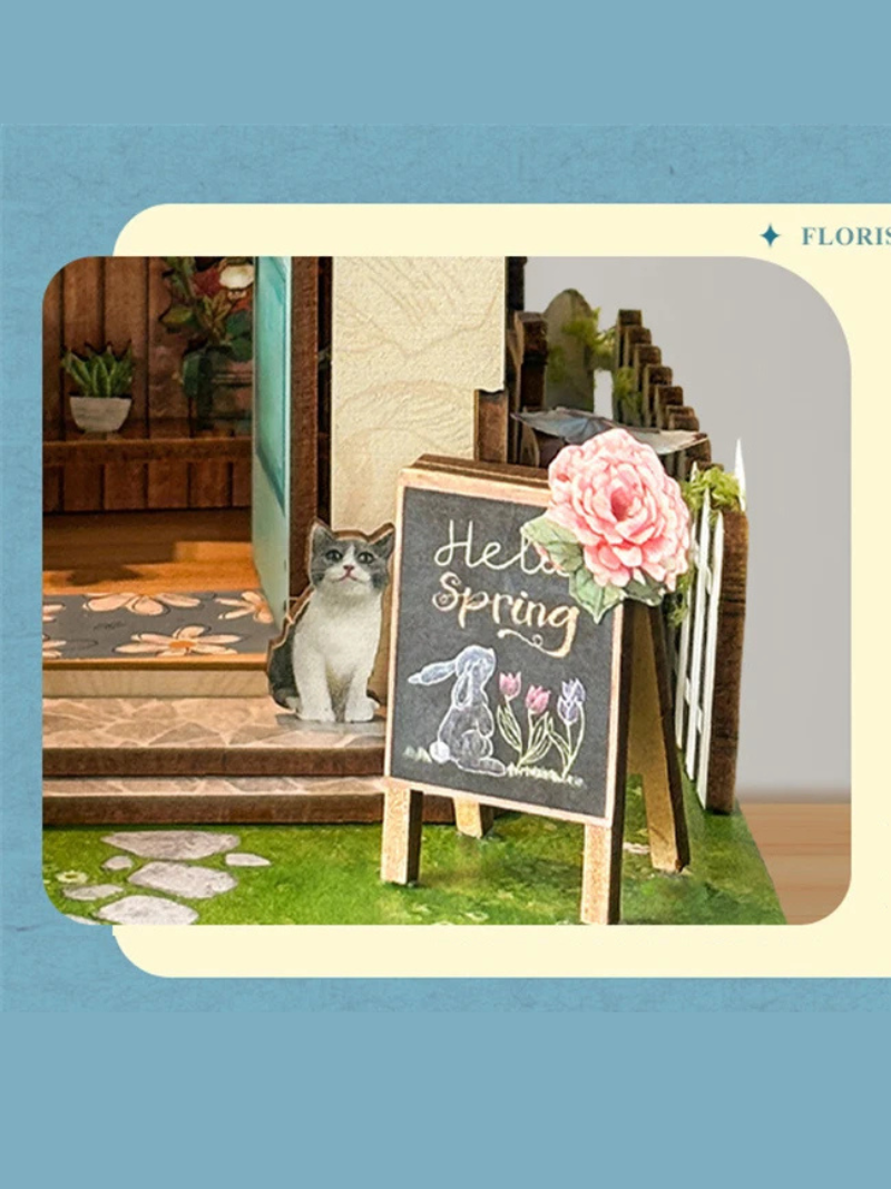 DIY book nook kit “Springkeeper’s Shop” featuring a cheerful miniature flower store with potted plants, blooming flowers, a striped awning, and a small cat. A charming craft idea for DIY and crafts lovers, perfect for fans of miniatures and DIY tiny home kits.