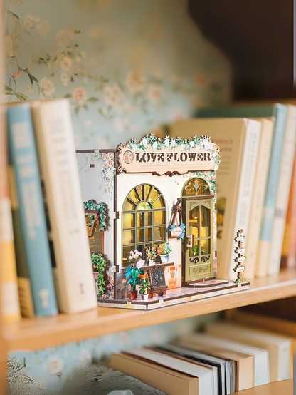DIY book nook kit “Maison de Fleurs,” featuring a pastel-toned miniature flower shop with arched windows, blooming plants, stone accents, and romantic signage. A relaxing DIY and crafts project for fans of tiny dollhouses and garden-inspired scenes.