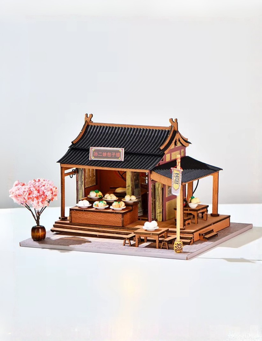 DIY mini house kit “Little Bao Shop,” featuring a traditional Chinese dumpling stand with miniature steamed buns, wooden tables, hanging signs, and a cherry blossom tree—perfect for DIY food miniatures and cultural craft ideas.