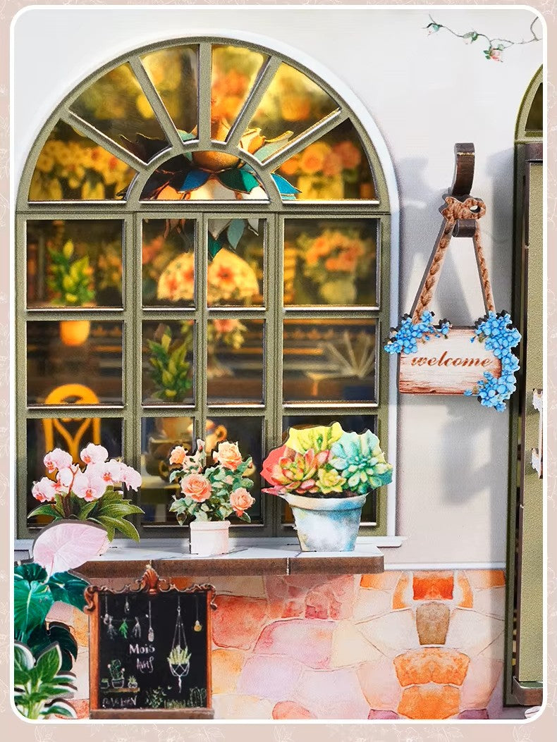 DIY book nook kit “Maison de Fleurs,” featuring a pastel-toned miniature flower shop with arched windows, blooming plants, stone accents, and romantic signage. A relaxing DIY and crafts project for fans of tiny dollhouses and garden-inspired scenes.