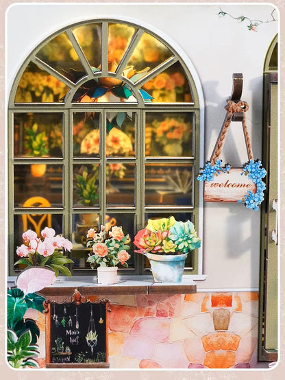DIY book nook kit “Maison de Fleurs,” featuring a pastel-toned miniature flower shop with arched windows, blooming plants, stone accents, and romantic signage. A relaxing DIY and crafts project for fans of tiny dollhouses and garden-inspired scenes.