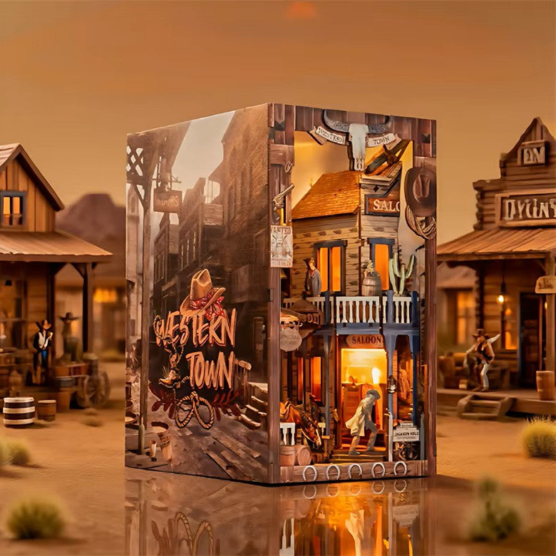 DIY miniature book nook of a Wild West street scene featuring a saloon façade with swinging doors, wooden signage, warm lantern lighting, and rustic storefront details, evoking a classic frontier town at dusk.