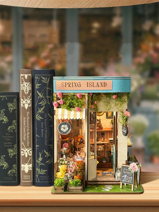 DIY book nook kit “Springkeeper’s Shop” featuring a cheerful miniature flower store with potted plants, blooming flowers, a striped awning, and a small cat. A charming craft idea for DIY and crafts lovers, perfect for fans of miniatures and DIY tiny home kits.