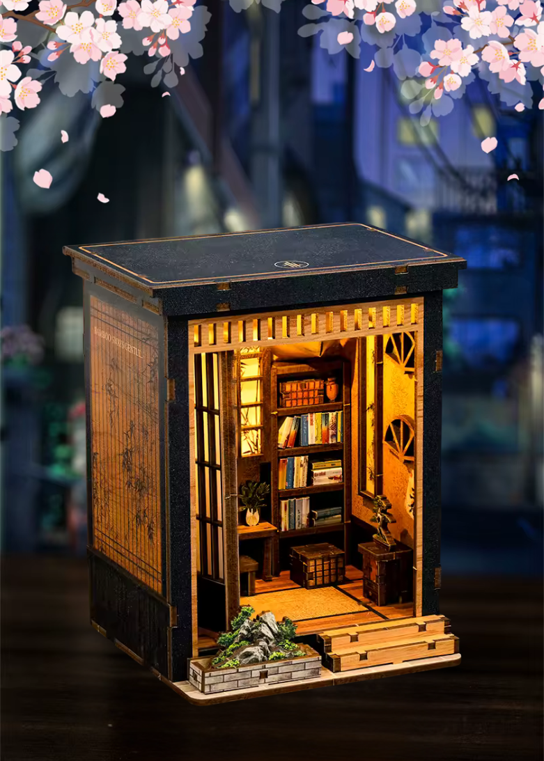 DIY book nook of a Japanese-style tea alcove featuring a glowing paper lantern, bonsai rock garden, shoji screen doors, bookshelves, and a peaceful wooden table, evoking the quiet ambiance of a neighborhood tea house.