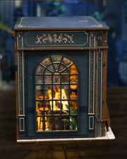 Miniature DIY book nook of a dark vintage-style café with glowing warm lights, ornate black storefront, and a coffee sign that reads “Jadeite Coffee.”
