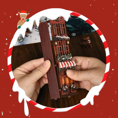 DIY book nook kit “Merry Market Lane,” featuring a warmly lit winter street with festive storefronts, snow-topped rooftops, and a softly bustling holiday vibe. A detailed DIY and crafts project perfect for holiday lovers and miniature collectors.