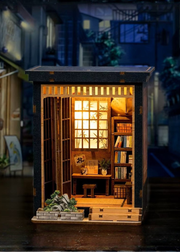 DIY book nook of a Japanese-style tea alcove featuring a glowing paper lantern, bonsai rock garden, shoji screen doors, bookshelves, and a peaceful wooden table, evoking the quiet ambiance of a neighborhood tea house.