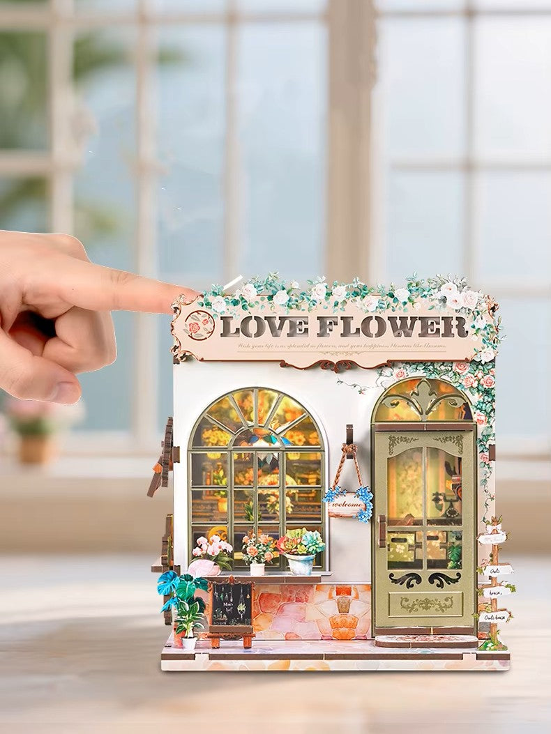 DIY book nook kit “Maison de Fleurs,” featuring a pastel-toned miniature flower shop with arched windows, blooming plants, stone accents, and romantic signage. A relaxing DIY and crafts project for fans of tiny dollhouses and garden-inspired scenes.