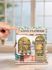 DIY book nook kit “Maison de Fleurs,” featuring a pastel-toned miniature flower shop with arched windows, blooming plants, stone accents, and romantic signage. A relaxing DIY and crafts project for fans of tiny dollhouses and garden-inspired scenes.