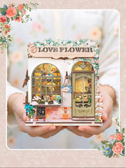 DIY book nook kit “Maison de Fleurs,” featuring a pastel-toned miniature flower shop with arched windows, blooming plants, stone accents, and romantic signage. A relaxing DIY and crafts project for fans of tiny dollhouses and garden-inspired scenes.
