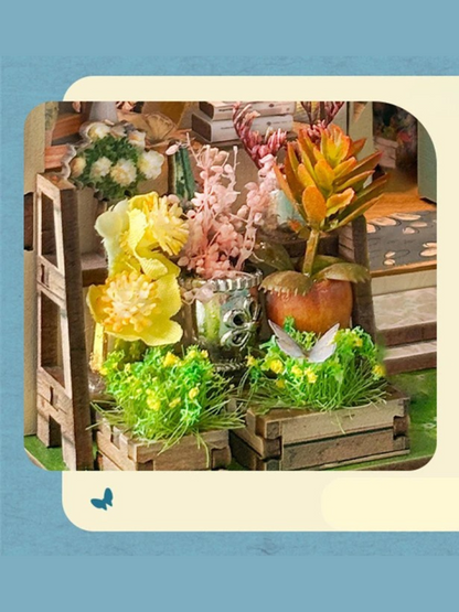 DIY book nook kit “Springkeeper’s Shop” featuring a cheerful miniature flower store with potted plants, blooming flowers, a striped awning, and a small cat. A charming craft idea for DIY and crafts lovers, perfect for fans of miniatures and DIY tiny home kits.