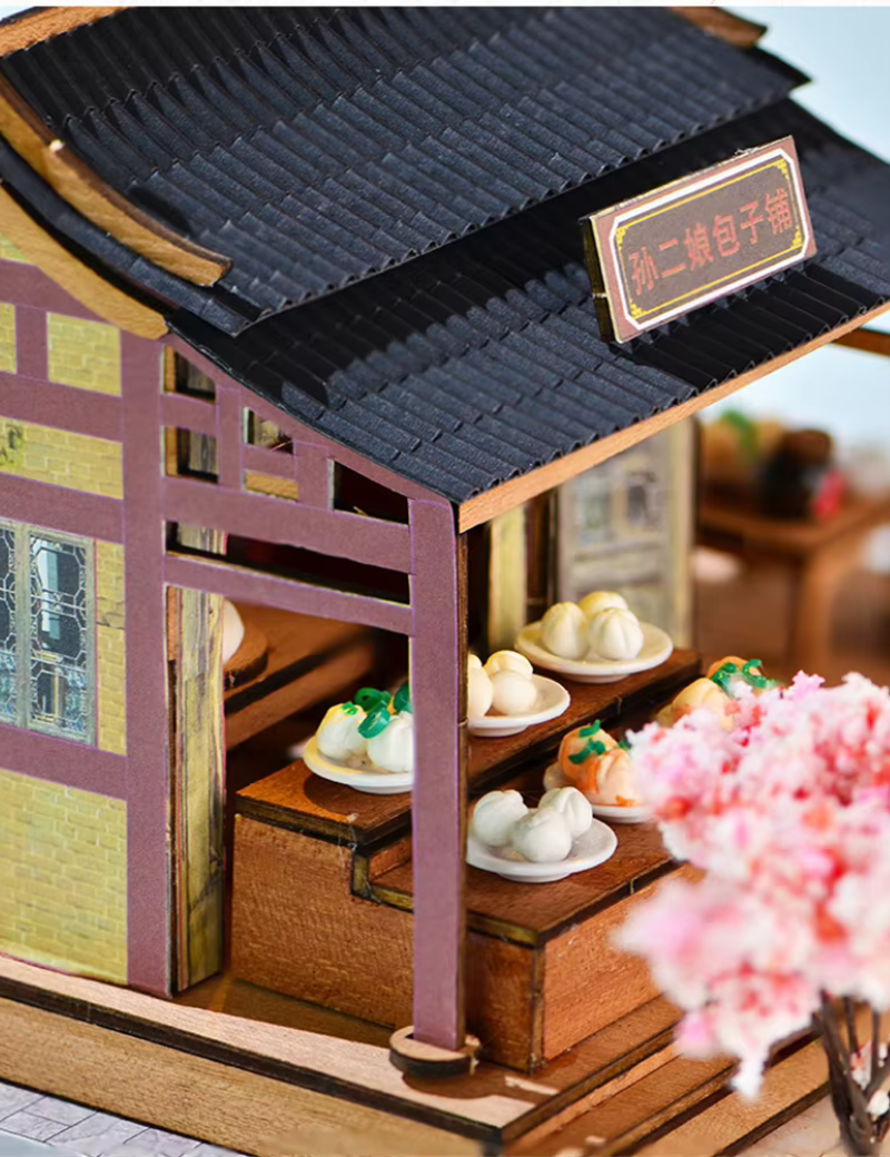 DIY mini house kit “Little Bao Shop,” featuring a traditional Chinese dumpling stand with miniature steamed buns, wooden tables, hanging signs, and a cherry blossom tree—perfect for DIY food miniatures and cultural craft ideas.