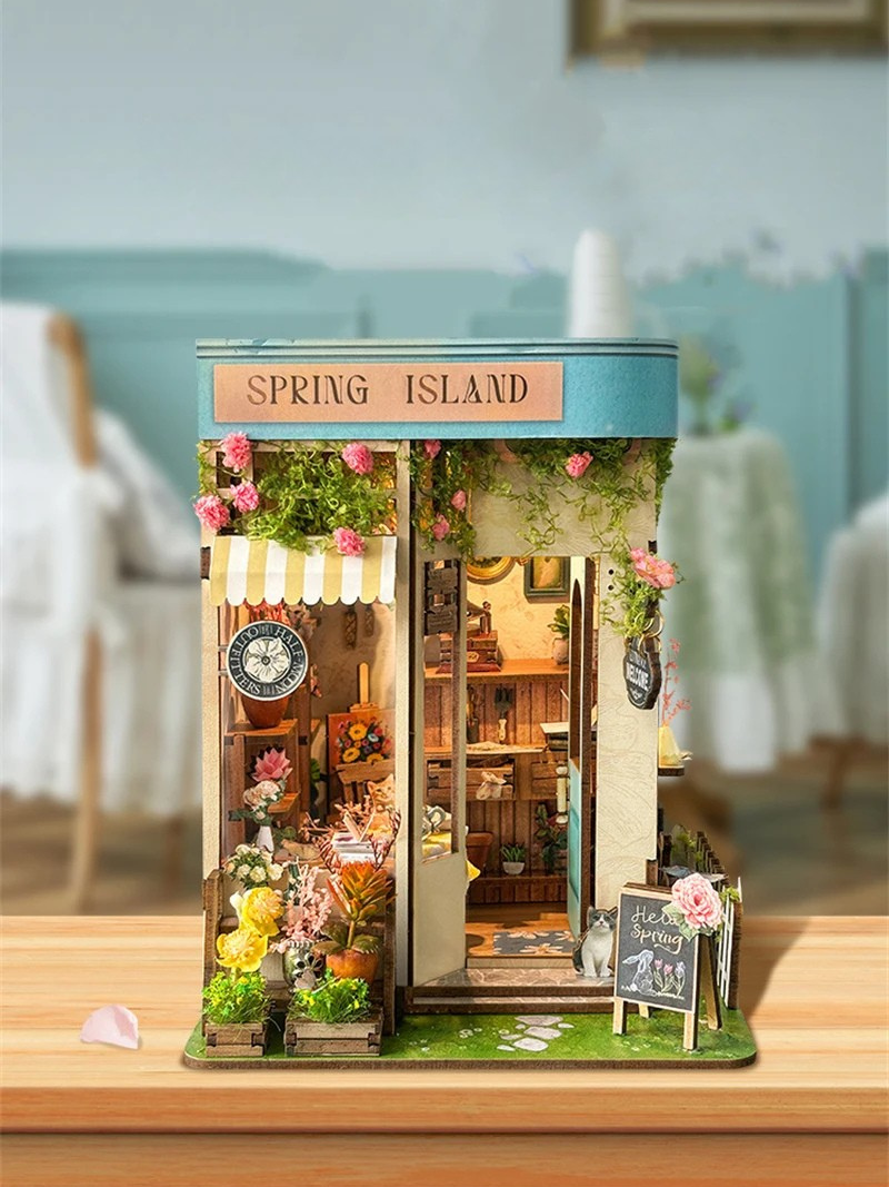 DIY book nook kit “Springkeeper’s Shop” featuring a cheerful miniature flower store with potted plants, blooming flowers, a striped awning, and a small cat. A charming craft idea for DIY and crafts lovers, perfect for fans of miniatures and DIY tiny home kits.