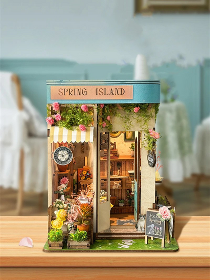 DIY book nook kit “Springkeeper’s Shop” featuring a cheerful miniature flower store with potted plants, blooming flowers, a striped awning, and a small cat. A charming craft idea for DIY and crafts lovers, perfect for fans of miniatures and DIY tiny home kits.