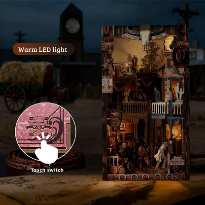 DIY miniature book nook of a Wild West street scene featuring a saloon façade with swinging doors, wooden signage, warm lantern lighting, and rustic storefront details, evoking a classic frontier town at dusk.