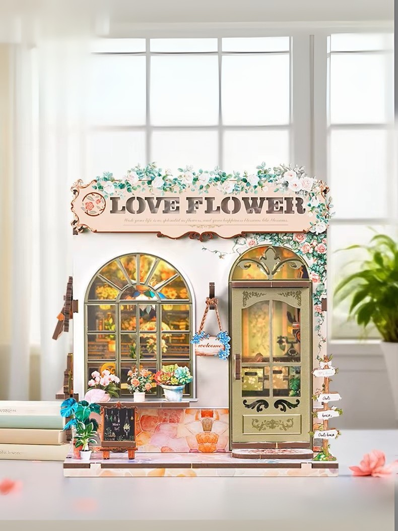 DIY book nook kit “Maison de Fleurs,” featuring a pastel-toned miniature flower shop with arched windows, blooming plants, stone accents, and romantic signage. A relaxing DIY and crafts project for fans of tiny dollhouses and garden-inspired scenes.