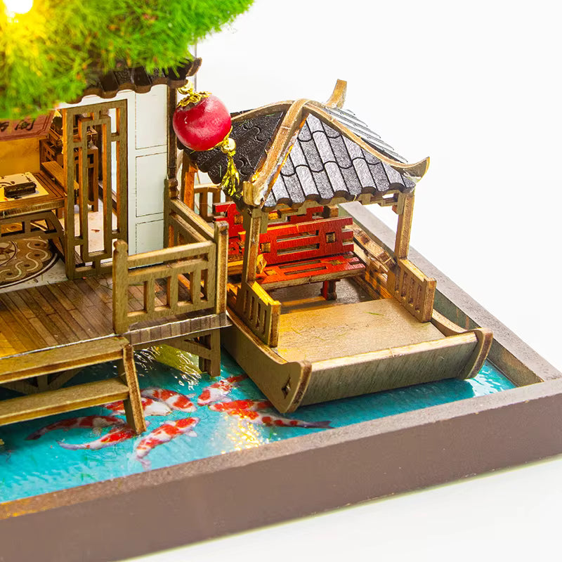 DIY miniature kit “Blossom Lantern Pavilion,” featuring a traditional East Asian-style building with curved roofs, cherry blossom trees, red lanterns, a waterfall, and glowing lights. A serene DIY and crafts project for fans of miniature homes and nature-inspired design.
