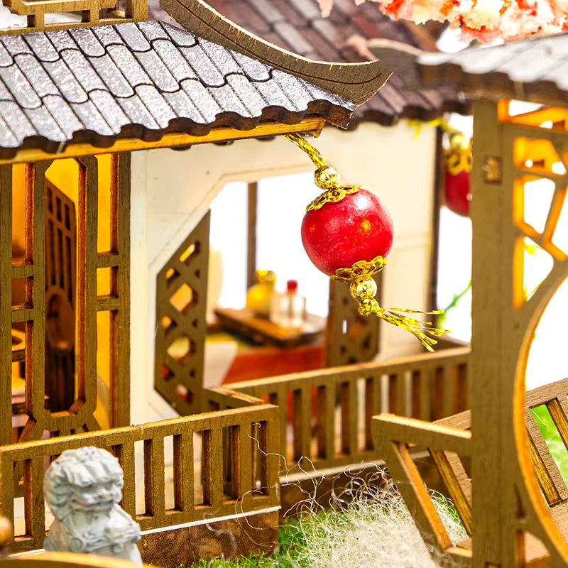 DIY miniature kit “Blossom Lantern Pavilion,” featuring a traditional East Asian-style building with curved roofs, cherry blossom trees, red lanterns, a waterfall, and glowing lights. A serene DIY and crafts project for fans of miniature homes and nature-inspired design.