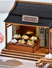DIY mini house kit “Little Bao Shop,” featuring a traditional Chinese dumpling stand with miniature steamed buns, wooden tables, hanging signs, and a cherry blossom tree—perfect for DIY food miniatures and cultural craft ideas.