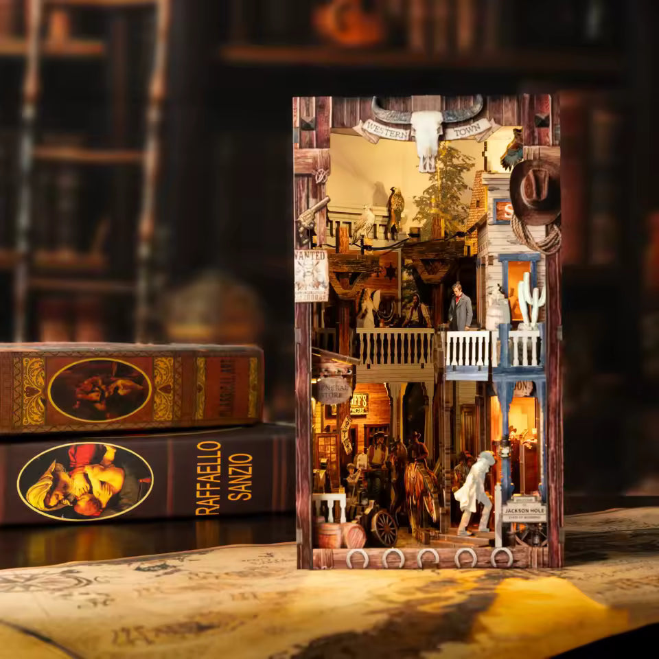 DIY miniature book nook of a Wild West street scene featuring a saloon façade with swinging doors, wooden signage, warm lantern lighting, and rustic storefront details, evoking a classic frontier town at dusk.