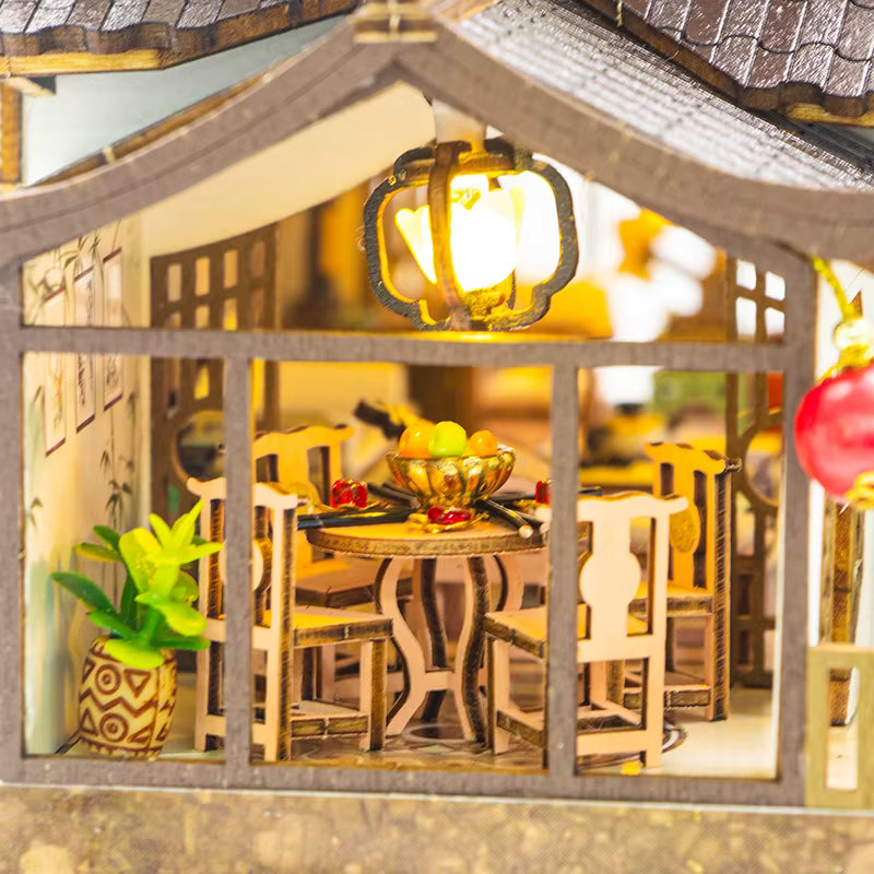 DIY miniature kit “Blossom Lantern Pavilion,” featuring a traditional East Asian-style building with curved roofs, cherry blossom trees, red lanterns, a waterfall, and glowing lights. A serene DIY and crafts project for fans of miniature homes and nature-inspired design.