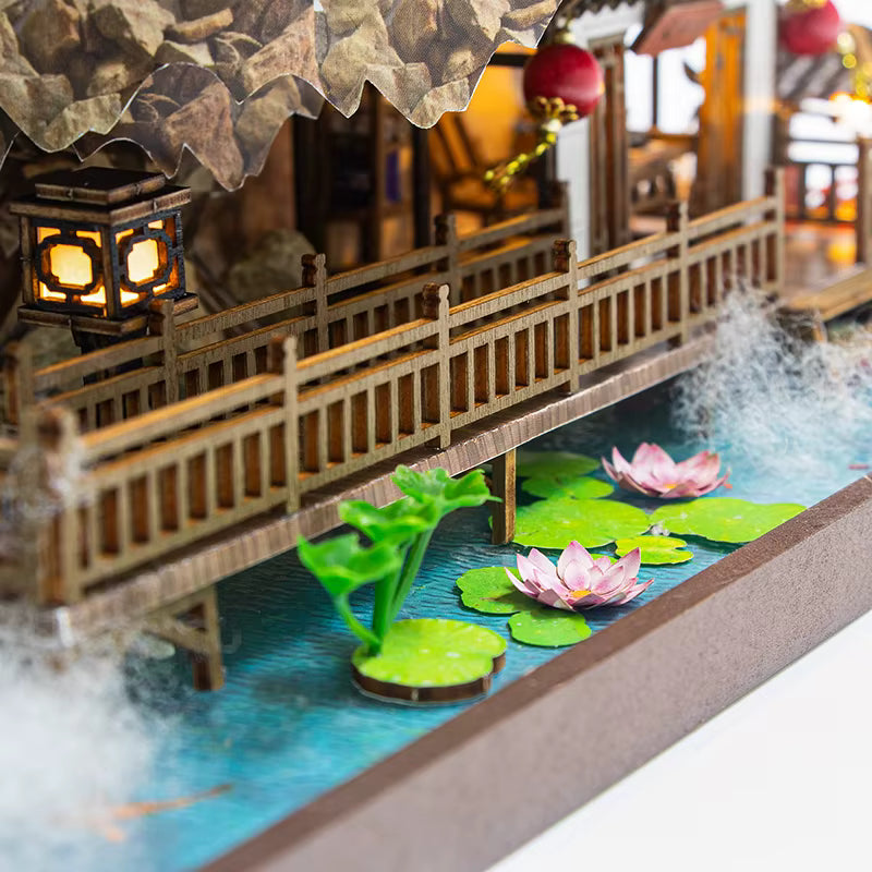 DIY miniature kit “Blossom Lantern Pavilion,” featuring a traditional East Asian-style building with curved roofs, cherry blossom trees, red lanterns, a waterfall, and glowing lights. A serene DIY and crafts project for fans of miniature homes and nature-inspired design.