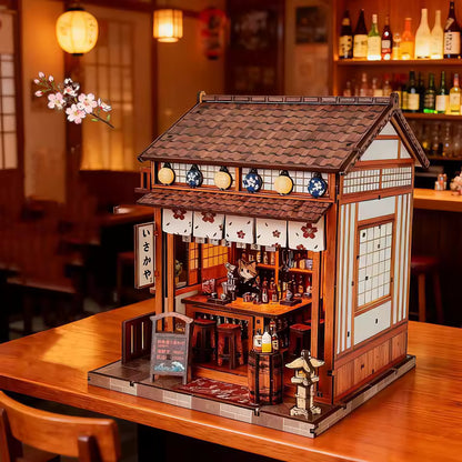 DIY miniature sake bar book nook with glowing lanterns, wooden bar seating, bamboo paneling, and rows of sake bottles, capturing the quiet atmosphere of a late-night Japanese tavern.