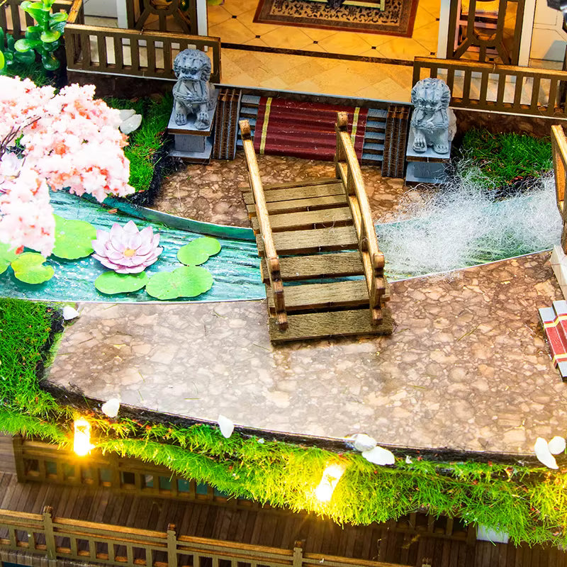 DIY miniature kit “Blossom Lantern Pavilion,” featuring a traditional East Asian-style building with curved roofs, cherry blossom trees, red lanterns, a waterfall, and glowing lights. A serene DIY and crafts project for fans of miniature homes and nature-inspired design.