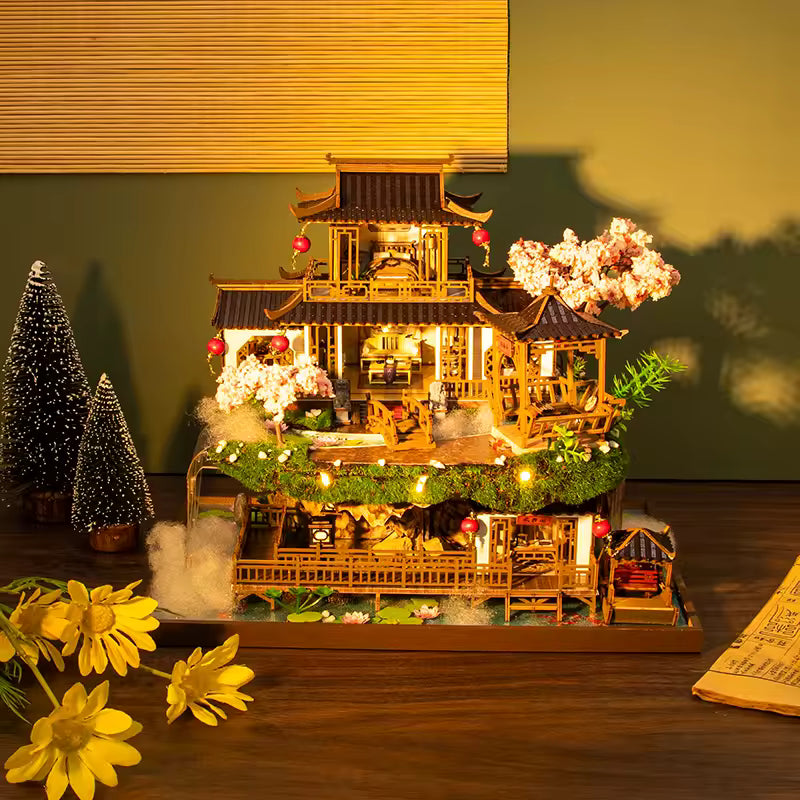 DIY miniature kit “Blossom Lantern Pavilion,” featuring a traditional East Asian-style building with curved roofs, cherry blossom trees, red lanterns, a waterfall, and glowing lights. A serene DIY and crafts project for fans of miniature homes and nature-inspired design.