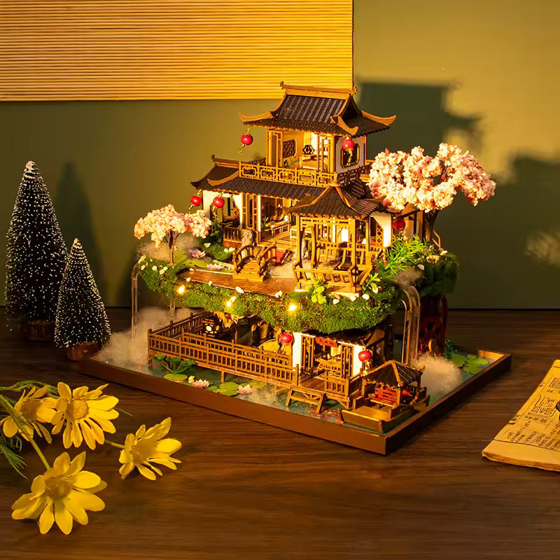 DIY miniature kit “Blossom Lantern Pavilion,” featuring a traditional East Asian-style building with curved roofs, cherry blossom trees, red lanterns, a waterfall, and glowing lights. A serene DIY and crafts project for fans of miniature homes and nature-inspired design.