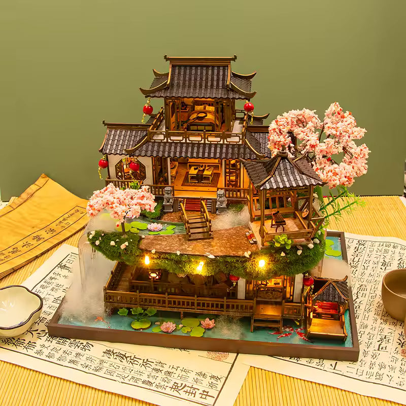DIY miniature kit “Blossom Lantern Pavilion,” featuring a traditional East Asian-style building with curved roofs, cherry blossom trees, red lanterns, a waterfall, and glowing lights. A serene DIY and crafts project for fans of miniature homes and nature-inspired design.