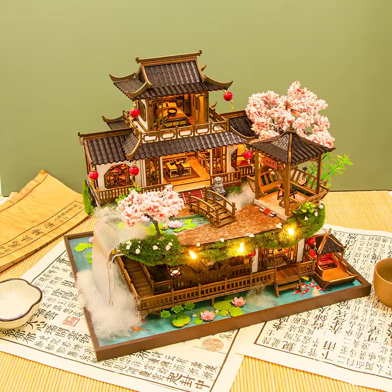 DIY miniature kit “Blossom Lantern Pavilion,” featuring a traditional East Asian-style building with curved roofs, cherry blossom trees, red lanterns, a waterfall, and glowing lights. A serene DIY and crafts project for fans of miniature homes and nature-inspired design.