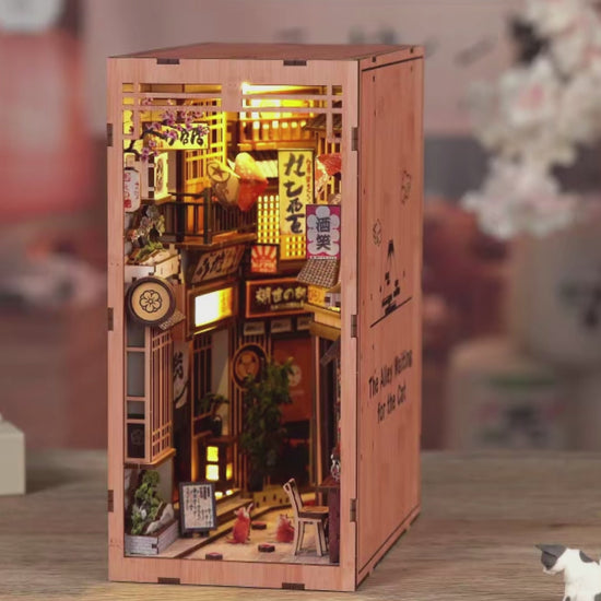 DIY book nook kit “Neko Alley Nook,” featuring a Japanese alleyway with miniature shopfronts, paper lanterns, wooden signage, and lounging cats. A charming DIY and crafts project for Japan enthusiasts and book nook collectors.