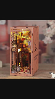DIY book nook kit “Neko Alley Nook,” featuring a Japanese alleyway with miniature shopfronts, paper lanterns, wooden signage, and lounging cats. A charming DIY and crafts project for Japan enthusiasts and book nook collectors.