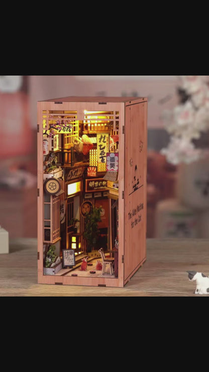 DIY book nook kit “Neko Alley Nook,” featuring a Japanese alleyway with miniature shopfronts, paper lanterns, wooden signage, and lounging cats. A charming DIY and crafts project for Japan enthusiasts and book nook collectors.