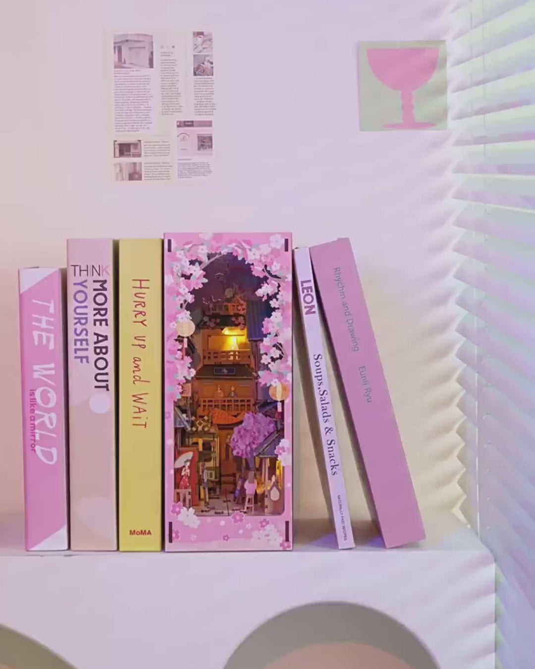 DIY book nook kit “Sakura Market,” featuring a glowing cherry blossom-lined miniature street scene with lanterns, shops, umbrellas, and Japanese architecture. Ideal for DIY and crafts lovers and fans of tiny dollhouses and book nook displays.